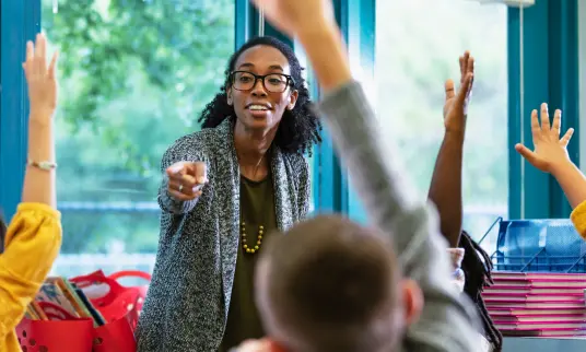 Female teacher calling on a student with their hand raised.